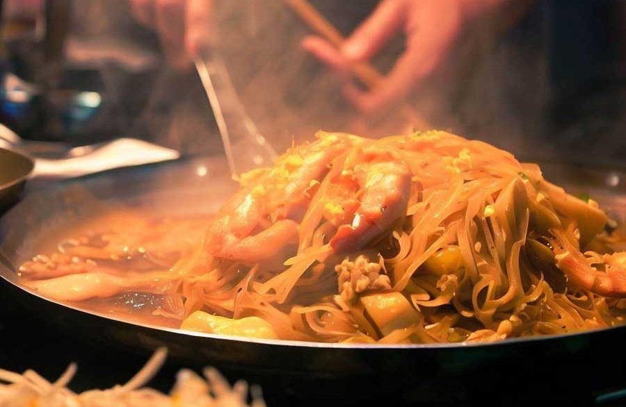 Plate of Pad Thai street food with rice noodles prawns peanuts and fresh lime wedges